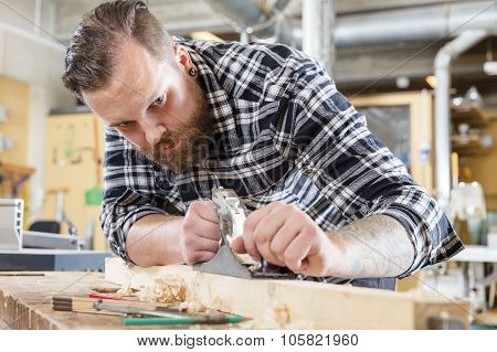 Focused carpenter work with plane on wood plank in workshop