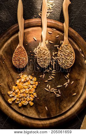 Top view of corn, millet, barley and oat grains in wooden spoons on round wooden tary