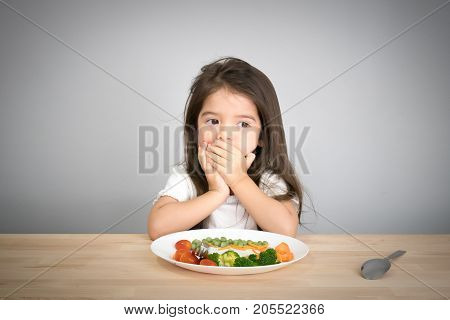 Nutrition & healthy eating habits for kids concept. Children do not like to eat vegetables. Little cute kid half race girl refuse to eat healthy vegetables.