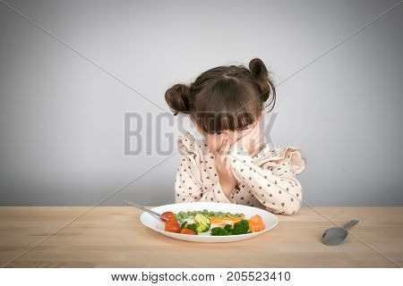 Nutrition & healthy eating habits for kids concept. Children do not like to eat vegetables. Little cute kid half race girl refuse to eat healthy vegetables.