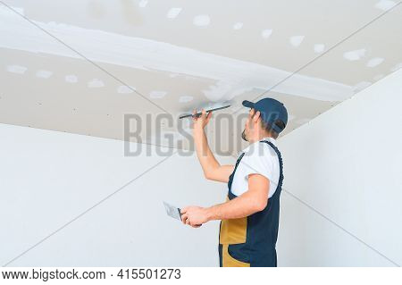 A Uniformed Worker Applies Putty To The Drywall Ceiling. Putty Of Joints Of Drywall Sheets.