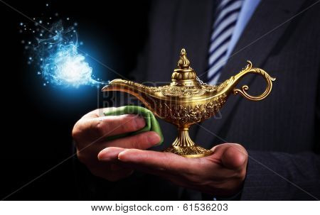 Businessman holding and rubbing a magic Aladdins genie lamp concept for business aspirations, hope and wishes