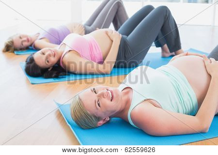 Happy pregnant women in yoga class lying on mats in a fitness studio