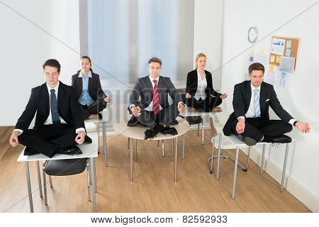 Meditating Businesspeople Sitting On Desk