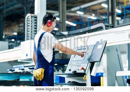 Worker entering data in CNC machine at factory floor to get the production going