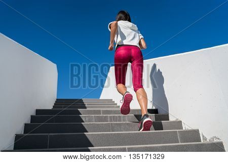 Stairs climbing running woman doing run up steps on staircase. Female runner athlete going up stairs in urban city doing cardio sport workout run outside during summer. Activewear leggings and shoes.