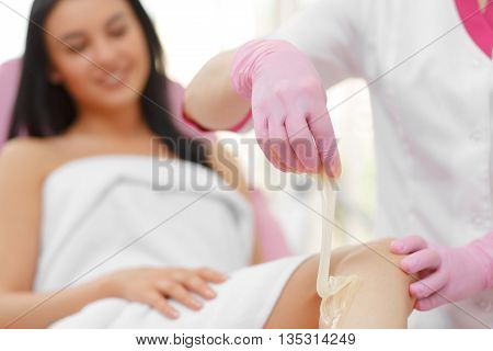 Sugaring: Beauty Concept. Hair removal on legs. Young beautiful girl with dark hair gets the procedure for hair removal liquid sugar. Beautician Giving Epilation To Woman On Thigh