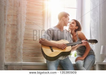 Happy couple in love. Stunning sensual portrait of young stylish fashion couple indoors. Young man playing guitar for his beloved girl.