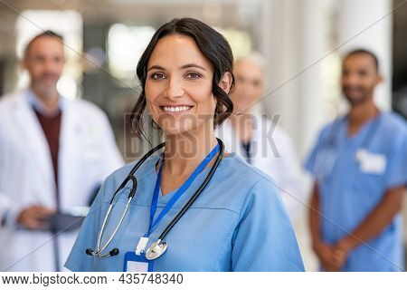 Portrait of happy young nurse in uniform with healthcare team in background. Successful team of doctor and nurses smiling. Beautiful and satisfied healthcare worker in private clinic looking at camera