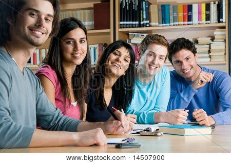 Joyeux groupe de jeunes étudiants étudient ensemble dans une bibliothèque de collège et regardant sourire caméra