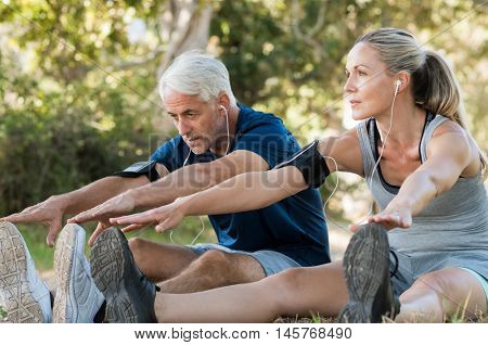 Mature couple stretching at park and listening to music. Athletic senior couple exercising together outdoor. Fit senior runners stretching before running outdoors. 