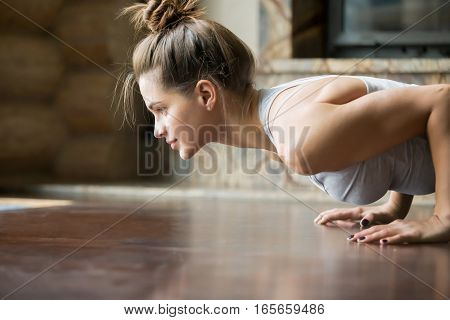 Closeup of young happy attractive woman practicing yoga, doing four limbed staff, push ups or press ups exercise, chaturanga dandasana pose, working out, wearing sportswear, bra, indoor, home interior