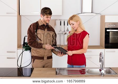 Young Smiling Woman Signing Invoice From Exterminator Worker After Pest Control Work In House Kitchen