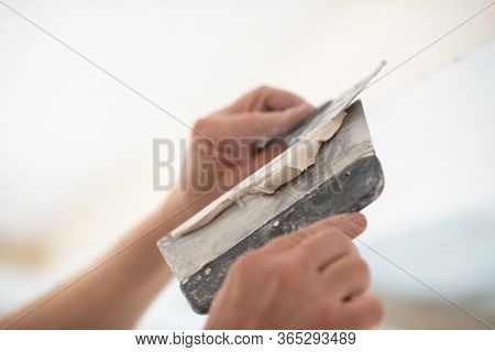 Worker putsty plasterboard ceiling in new building. Repairman works with plasterboard, plastering dry-stone wall, home improvement. A man makes repairs at home. Putty knife in male hand