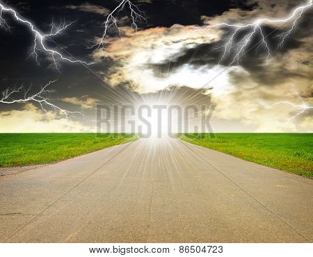 Old road, roadsides and green grass field. Stormy sky with lightning in background