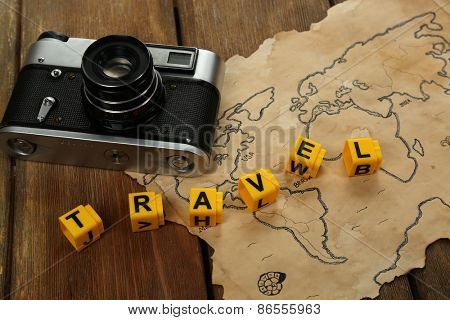 Retro camera on world map with word Travel on wooden table background