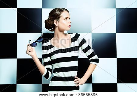 Beautiful fashion model posing in dress in black and white stripes on a background of black and white squares. Beauty, fashion concept. Business style.