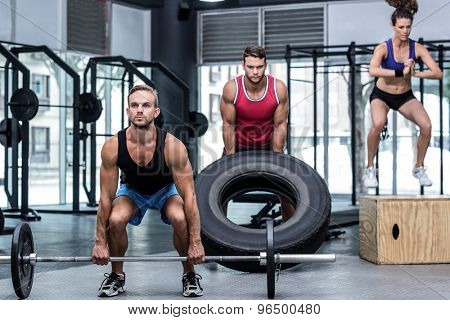 Three muscular athletes lifting and jumping at the crossfit gym