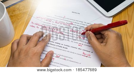 hand holding red pen over proofreading text on table