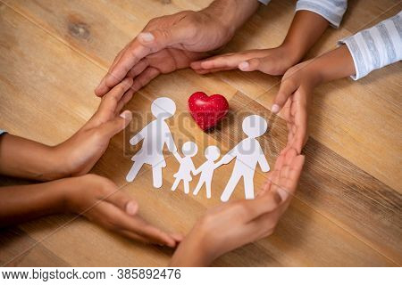 Close up hands of father, mother and daughters protecting family paper cutout with red heart. Hands of family with paper cutting and red heart shaped symbol stone. Unity, insurance and love concept.