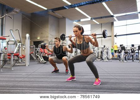 sport, bodybuilding, lifestyle and people concept - young man and woman with barbell flexing muscles and making shoulder press squat in gym