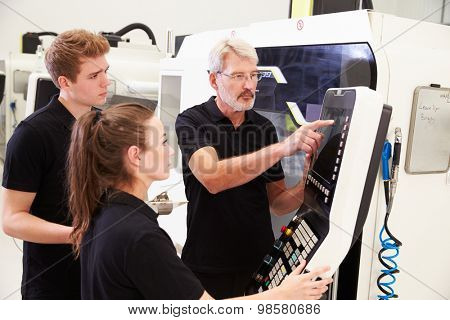 Two Apprentices Working With Engineer On CNC Machinery