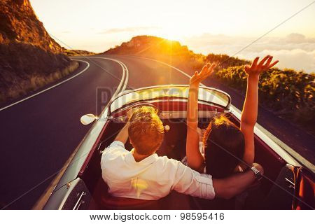 Happy Couple Driving on Country Road into the Sunset in Classic Vintage Sports Car 