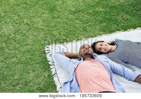 Young multiethnic couple lying on blanket on grass. Latin woman with her african boyfriend relaxing on picnic blanket outdoor. Mature happy couple in love lying on grass with copy space.