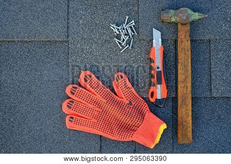 Close Up View On Bitumen Asphalt Shingles On A Roof  With Hammer,nails And Stationery Knife. Use Of 