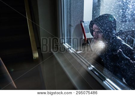 Burglar With Crowbar And Flashlight Looking Into A House Windows