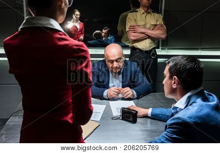 Middle-aged man thinking about his statement and the criminal charge while sitting down during interrogation in the office of the police station