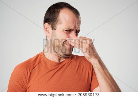 Caucasian man is pinching nose with fingers and looking with disgust because of bad smell isolated on white background. Negative human face expression body language reaction