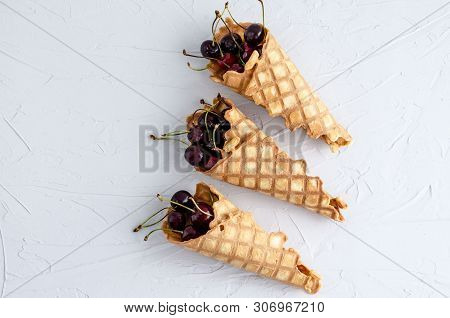 Ice Cream Cone Filled With Cherries On A Light White Concrete Background.