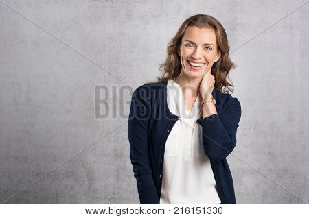 Cheerful mid adult woman laughing and looking at camera. Portrait of smiling businesswoman enjoying standing against grey wall. Happy mature woman looking at camera with toothy smile, copyspace.