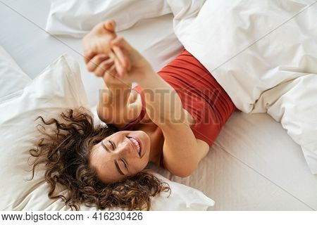 Top view of cheerful woman waking up after sleep and stretching on bed. High angle view of beautiful girl lying on bed and stretching after wake up. Awake woman wake up in morning and feeling fresh.