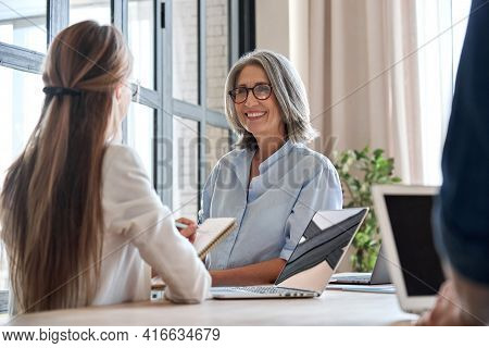 Happy Mature Middle 60s Aged Smiling Lady Boss Manager Teacher Talking To Assistant Or Student Meeti