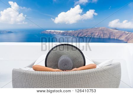 Travel vacation woman relaxing enjoying Santorini looking at famous view of Caldera. Young lady lying down on sun bed sofa lounge chair on holidays. Amazing view of sea. Europe travel destination.