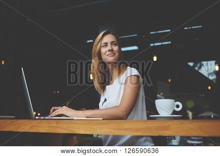 Young gorgeous European woman with pretty face thinking about something while sitting with laptop computer in cafe bar dreamy beautiful female using portable net-book during work break in coffee shop