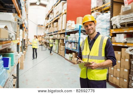 Warehouse worker smiling at camera with clipboard in a large warehouse