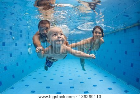 Happy full family - mother father baby son learn to swim dive underwater with fun in pool to keep fit. Healthy lifestyle active parent people water sport activity swimming lesson. Focus on child