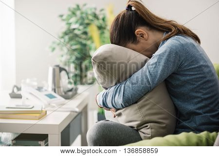 Unhappy lonely depressed woman at home she is sitting on the couch and hiding her face on a pillow depression concept