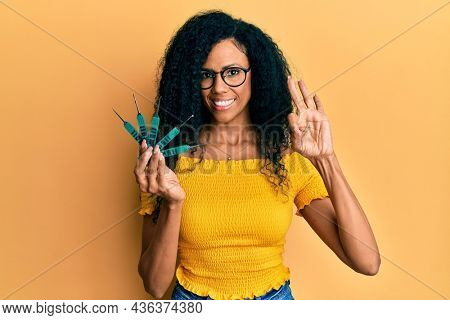 Middle age african american woman holding picklock to unlock security door doing ok sign with fingers, smiling friendly gesturing excellent symbol 