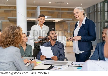 Group of business people discussing work in conference room. Senior business manager guiding employees in meeting. Group of businessman and businesswoman working together while sharing new strategy.