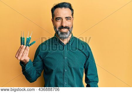 Middle age man with beard and grey hair holding picklock to unlock security door looking positive and happy standing and smiling with a confident smile showing teeth 