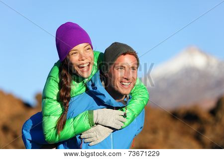 Couple piggyback happy in active lifestyle having fun on hike. Fresh young joyful interracial couple. Asian woman hiker and Caucasian man in outdoor activity on Teide, Tenerife, Canary Islands, Spain