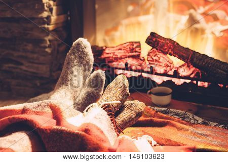 Cold fall or winter evening. People resting by the fire with blanket and tea. Closeup photo of feet in woolen socks. Cozy scene.