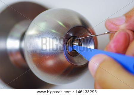 Closeup hands of locksmith using pick tools to open locked door.