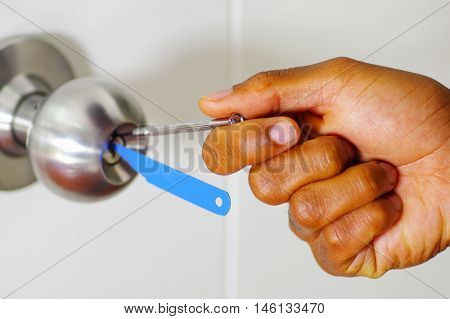 Closeup hands of locksmith using pick tools to open locked door.