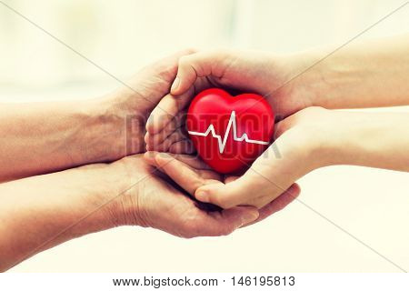 charity, health care, donation and medicine concept - man hand giving red heart with cardiogram to woman