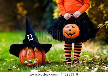 Little girl in witch costume playing in autumn park. Child having fun at Halloween trick or treat. Kids trick or treating. Toddler kid with jack-o-lantern. Children with candy bucket in fall forest.